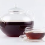 Gläserne Teekanne mit dunklem Tee und Glastasse auf weißem Hintergrund