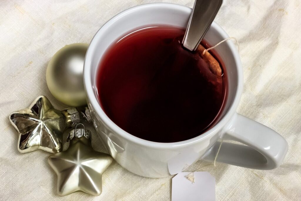 Weiße Tasse mit rotem Früchtetee neben silbernen Weihnachtssternen