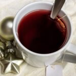 Weiße Tasse mit rotem Früchtetee neben silbernen Weihnachtssternen