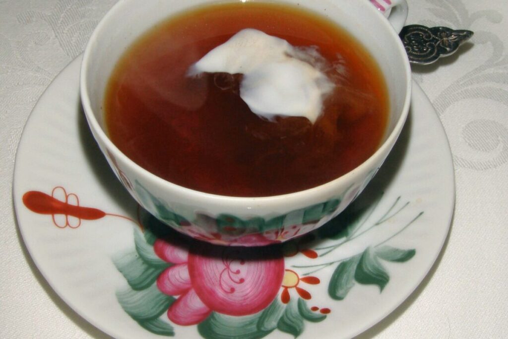 Tasse Ostfriesentee mit Sahnewolke auf einer Untertasse mit Rosendekor