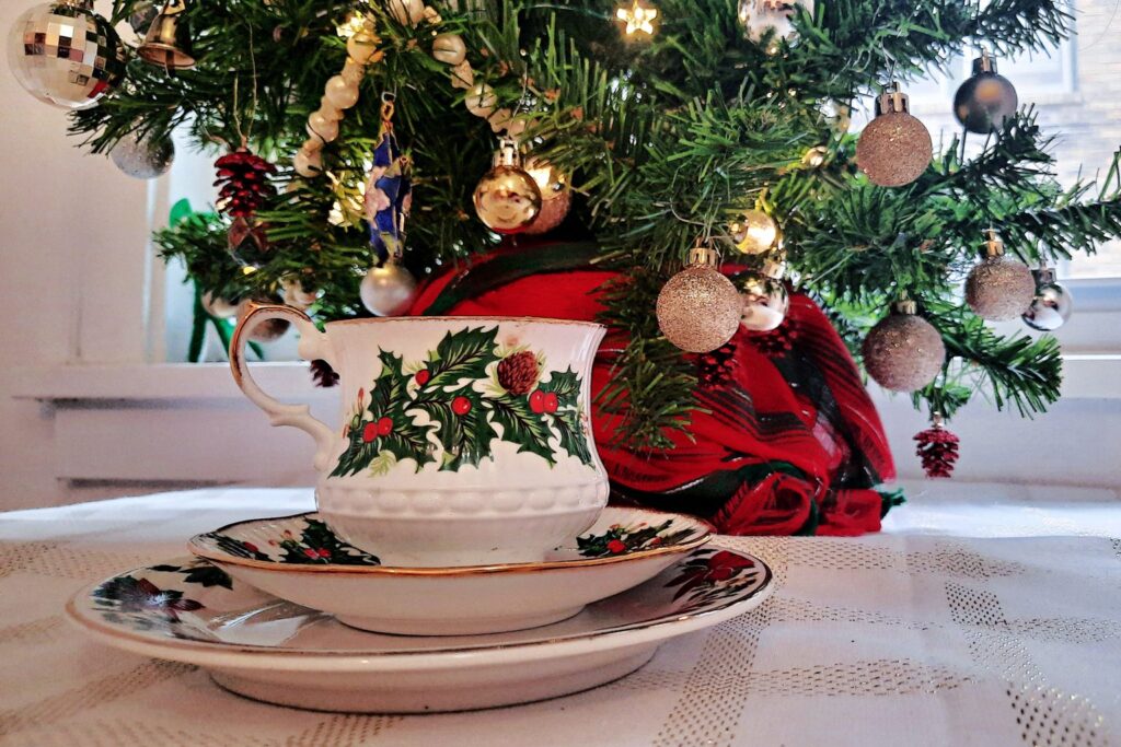 Weihnachtliche Teetasse mit Stechpalmen-Dekor vor einem geschmückten Tannenbaum