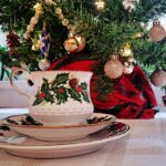 Weihnachtliche Teetasse mit Stechpalmen-Dekor vor einem geschmückten Tannenbaum