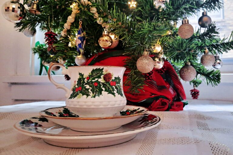 Weihnachtliche Teetasse mit Stechpalmen-Dekor vor einem geschmückten Tannenbaum