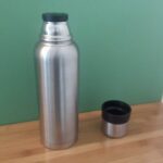 Silberne Edelstahl-Thermosflasche mit abgenommenem Becher auf einer Holzarbeitsplatte