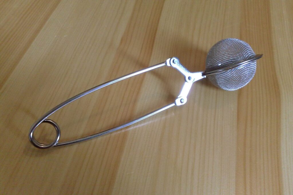 Teesieb-Zange aus Edelstahl auf einer hellen Holzoberfläche