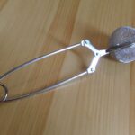 Teesieb-Zange aus Edelstahl auf einer hellen Holzoberfläche
