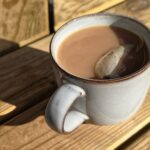 Keramiktasse mit Tee auf einem sonnenbeschienenen Holztisch